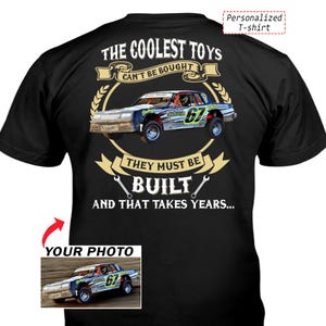 May include: A black t-shirt featuring a graphic of a race car with the number 67. The text reads: THE COOLEST TOYS CAN'T BE BOUGHT THEY MUST BE BUILT AND THAT TAKES YEARS. A smaller inset box shows the same race car with the text YOUR PHOTO.