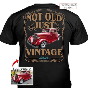 Op de afbeelding: Een zwart t-shirt met een afbeelding van een rode oldtimer. De tekst luidt NOT OLD JUST VINTAGE Authentic 100 PROOF. Het ontwerp is omgeven door een decoratieve beige rand. Een klein kader toont dezelfde auto met de tekst YOUR PHOTO.