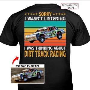 May include: A black t-shirt featuring a graphic of a race car with the number 67. The text reads SORRY I WASN'T LISTENING I WAS THINKING ABOUT DIRT TRACK RACING. The design includes a retro-style sunset background and a space for a custom photo.