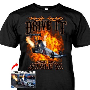 May include: Black t-shirt featuring a drag racing car engulfed in flames. The text "DRIVE IT LIKE YOU STOLE IT" is displayed in orange and black. A small image of a drag race car is in the lower left corner.