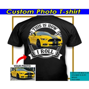 Puede incluir: Una camiseta negra con un gráfico blanco de un Ford Mustang amarillo con rayas de carreras negras. El gráfico incluye el texto "This is how I roll". La camiseta es personalizable con tu propia foto de un coche.