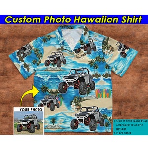 Puede incluir: Una camisa hawaiana azul con fondo blanco que presenta un patrón repetido de palmeras, olas del océano y vehículos todoterreno. La camisa tiene un cuello blanco y mangas cortas. El texto "Custom Photo Hawaiian Shirt" está en la parte superior de la imagen. El texto "YOUR PHOTO" está en un cuadro blanco con una flecha blanca que apunta hacia la derecha. El cuadro contiene una imagen más pequeña de una camisa similar con un vehículo todoterreno diferente.