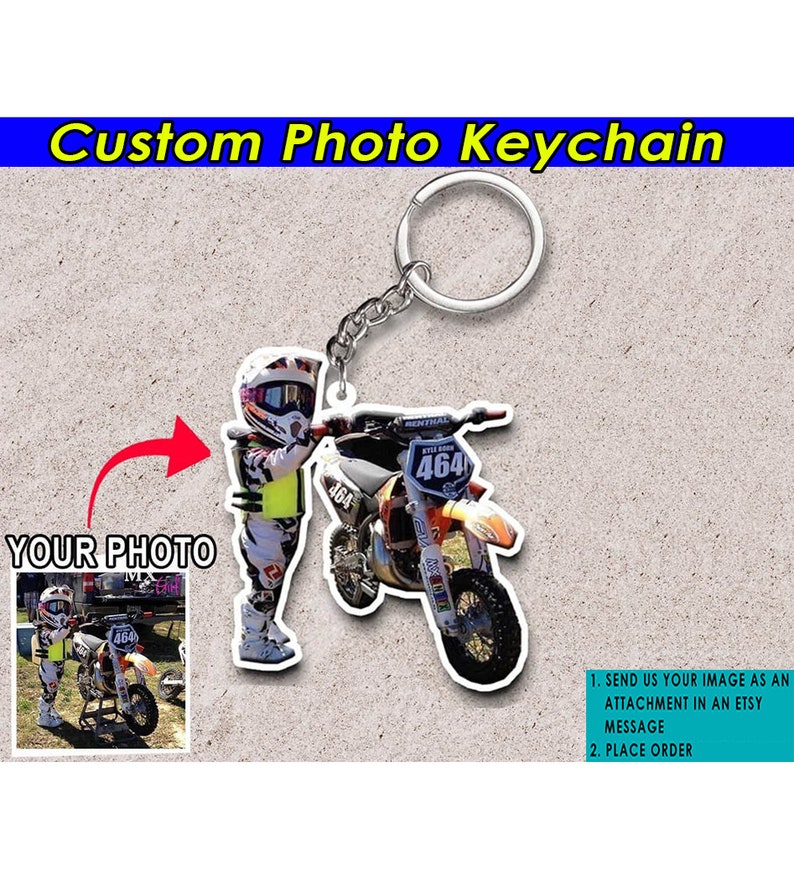 May include: A custom photo keychain featuring a child in a motocross racing suit holding a dirt bike. The keychain is made of clear acrylic and has a silver metal key ring.