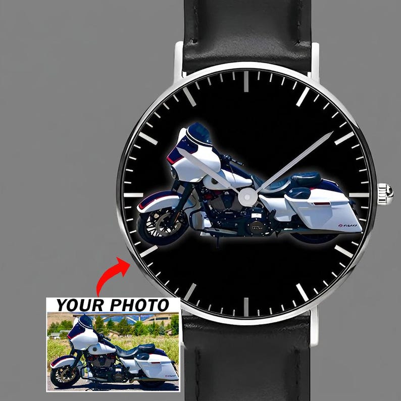 May include: A round analog wristwatch with a black leather strap and a silver-toned case. The watch face features a black background with a white motorcycle graphic and silver hands. A small inset shows a photo of the same white motorcycle.