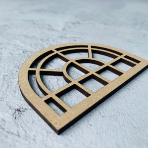 Op de afbeelding: Een houten uitsnijding van een halfronde venster met een geometrisch ontwerp. Het venster is gemaakt van meerdere vierkanten en rechthoeken.