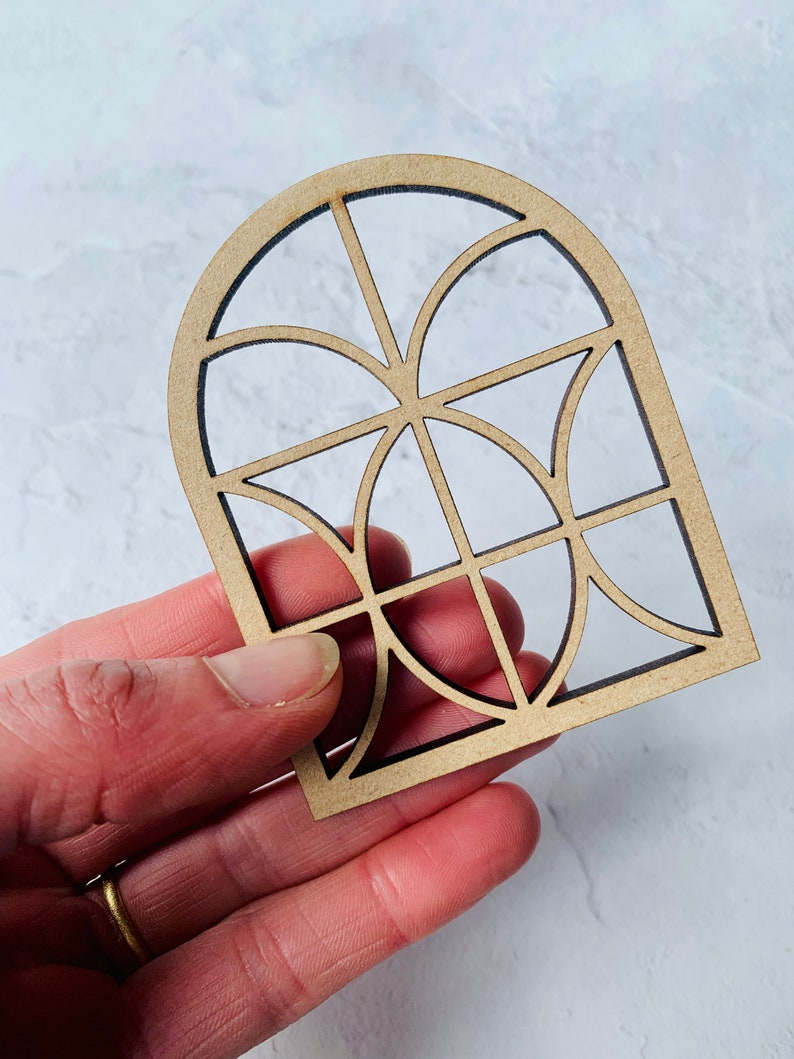 Op de afbeelding: Een houten uitsnijding van een gebogen raam met een geometrisch ontwerp. Het raam is gemaakt van dun hout en heeft een lichtbruine kleur.