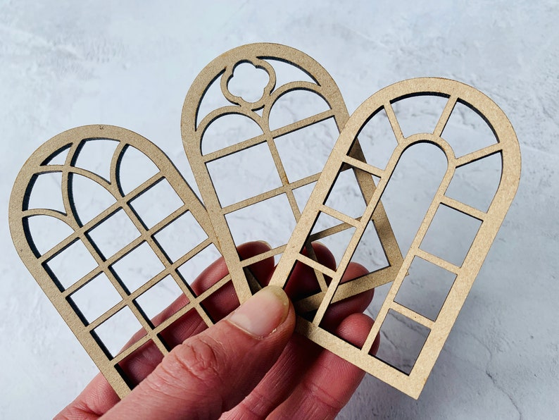 Op de afbeelding: Drie houten raamkozijnen met verschillende ontwerpen. De kozijnen zijn gemaakt van lichtbruin hout en hebben een verweerde afwerking. De kozijnen zijn perfect voor knutselprojecten, woonaccessoires of scrapbooking.