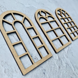 Op de afbeelding: Drie houten boogvensterframes met verschillende ruitpatronen. De frames zijn gemaakt van lichtbruin hout en hebben een rustieke uitstraling.