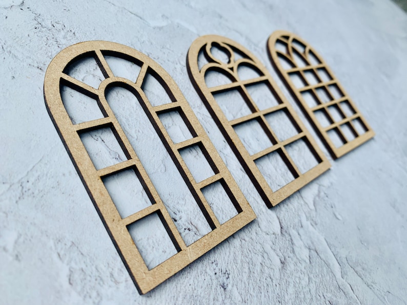 Op de afbeelding: Drie houten boogvensterframes met verschillende ruitpatronen. De frames zijn gemaakt van lichtbruin hout en hebben een rustieke uitstraling.