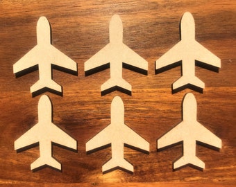 May include: Six wooden airplane shapes, all the same size and design, are arranged in two rows of three on a brown wooden surface. The airplanes are cut out of a light brown wood and have a simple, classic design.