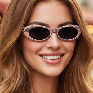 May include: Oval-shaped sunglasses with a snakeskin pattern frame and dark lenses. The sunglasses are a light pink and brown color. The person in the image is smiling.
