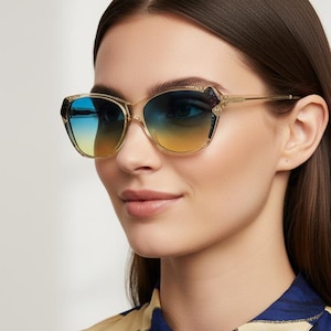 May include: Gold-framed sunglasses with gradient blue and yellow lenses. The sunglasses have a cat-eye shape with decorative accents on the corners. The woman is wearing a blue and beige patterned blouse.