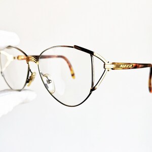 Op de afbeelding: Gouden metalen bril met een schildpadaccent op de pootjes. De monturen hebben een cat-eye vorm met een dun, delicaat ontwerp.