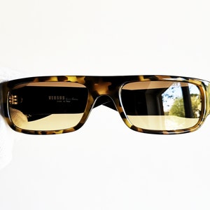 May include: Tortoiseshell sunglasses with brown lenses. The sunglasses have a square frame and the brand name 'VERSUS' is printed on the left lens.