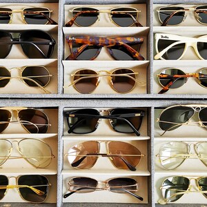 Pu&ograve; includere: Una vetrina con 12 paia di occhiali da sole in vari stili e colori. Gli occhiali da sole sono disposti in file di tre, con ogni fila che presenta uno stile diverso.