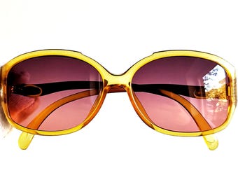 May include: A pair of amber-coloured plastic sunglasses with brown lenses. The sunglasses have a rounded, oval shape.