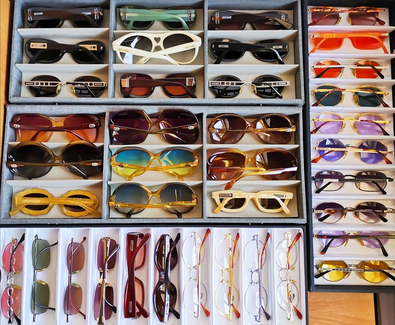 Puede incluir: Una colecci&oacute;n de gafas de sol y gafas graduadas en varios estilos y colores, expuestas en bandejas organizadas. El surtido incluye monturas con detalles en negro, marr&oacute;n y dorado, as&iacute; como lentes de colores.