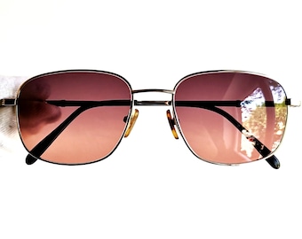 May include: A pair of gold-rimmed sunglasses with brown lenses. The sunglasses have a classic aviator style.