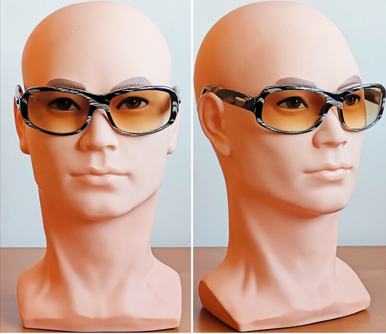 Puede incluir: Gafas de sol rectangulares con montura estampada en blanco y negro y lentes degradadas en naranja. Las gafas se exhiben en una cabeza de maniqu&iacute;. Las monturas tienen un aspecto texturizado y las lentes pasan de un naranja m&aacute;s oscuro en la parte superior a un tono m&aacute;s claro.