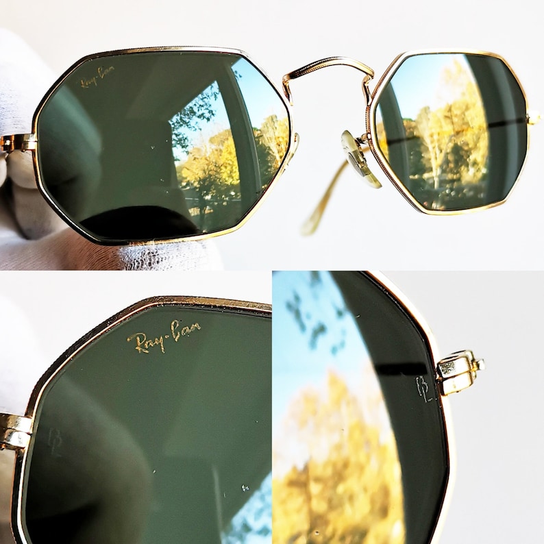 Pu&ograve; includere: Occhiali da sole Ray-Ban dorati con lenti verdi e montatura esagonale. Gli occhiali si riflettono nelle lenti, mostrando una vista di alberi e un edificio.