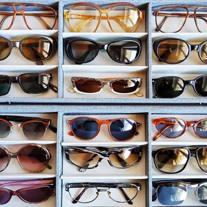 Puede incluir: Una colecci&oacute;n de gafas de sol y gafas graduadas en una caja de almacenamiento gris. Las gafas presentan varios estilos y colores de montura, incluyendo monturas marrones, negras, naranjas y transparentes. Las lentes tienen diferentes tonalidades, e incluye gafas de sol y gafas graduadas.