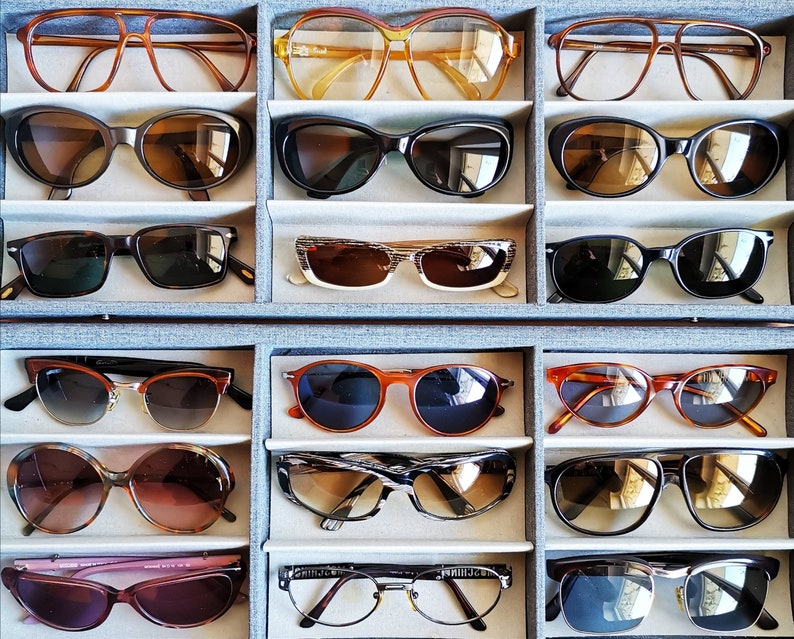Puede incluir: Una colecci&oacute;n de gafas de sol y gafas graduadas en una caja de almacenamiento gris. Las gafas presentan varios estilos y colores de montura, incluyendo monturas marrones, negras, naranjas y transparentes. Las lentes tienen diferentes tonalidades, e incluye gafas de sol y gafas graduadas.