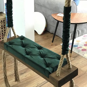 May include: A green velvet swing seat with a wooden frame and rope straps. The swing is hanging from the ceiling and has a tufted design.