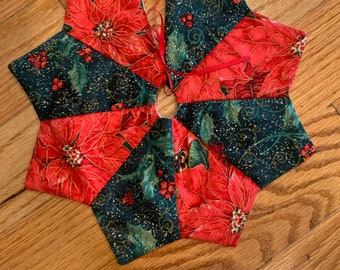 May include: A red and green Christmas tree skirt with a poinsettia pattern. The skirt is made of fabric and has a star shape.