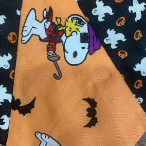 May include: Orange fabric with a black and white cartoon dog wearing a purple hat and holding a sword. The fabric has a pattern of bats, ghosts, and pumpkins.