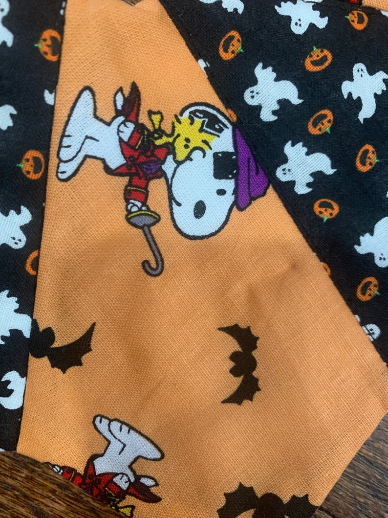 May include: Orange fabric with a black and white cartoon dog wearing a purple hat and holding a sword. The fabric has a pattern of bats, ghosts, and pumpkins.