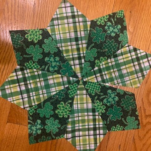 May include: A green and white plaid fabric star with a shamrock pattern. The star is made of eight points and is sewn together.