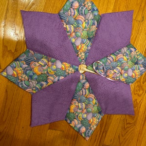 May include: Purple and green fabric star-shaped table topper with a pattern of colourful Easter eggs.