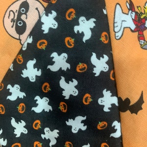 May include: A black and white fabric with a pattern of white ghosts and orange pumpkins. The fabric is part of a larger patchwork design with other Halloween themed fabrics.