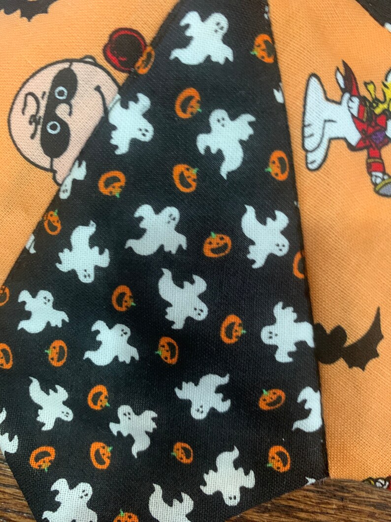 May include: A black and white fabric with a pattern of white ghosts and orange pumpkins. The fabric is part of a larger patchwork design with other Halloween themed fabrics.