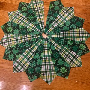 May include: A green and white plaid fabric tree skirt with a shamrock pattern. The skirt is made of 12 fabric pieces sewn together in a circle.