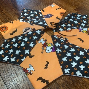 May include: A multi-colored fabric tree skirt with a black and white ghost and pumpkin pattern, an orange and black Peanuts pattern, and a black and white Peanuts pattern. The skirt has a black ribbon tied around the center.