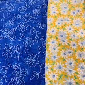 Könnte beinhalten: Zwei Stoffmuster, eines blau mit einem weißen Blumenmuster und Schmetterlingen, das andere gelb mit einem weißen Gänseblümchenmuster.