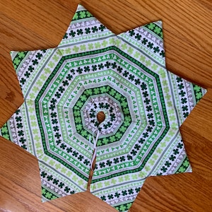 May include: A green and white star-shaped tree skirt with a shamrock pattern. The skirt has a hole in the center for the tree trunk.