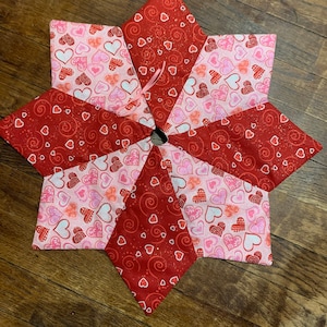 Puede incluir: Una falda de árbol de tela roja y rosa con un patrón de corazones. La falda está hecha de varias piezas de tela cosidas juntas para formar una estrella.