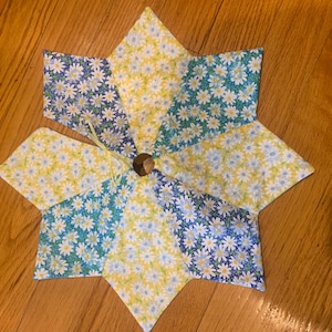 以下が含まれることがあります： 青、黄色、白のデイジー柄の布で作られた星型のテーブルランナーです。