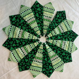 May include: A green and black tree skirt with a shamrock pattern. The skirt is made of fabric and has a scalloped edge.