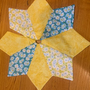 以下が含まれることがあります： デイジー柄の黄色と青の星形テーブルランナー。テーブルランナーは布製で、テーブル脚用の穴が中央にあります。