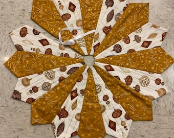 May include: A star-shaped Christmas tree skirt with alternating sections of gold and white fabric. The gold sections have a swirling pattern, while the white sections feature ornaments in brown and gold. A white ribbon is attached.