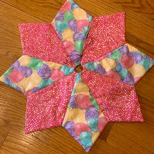 以下が含まれることがあります： 中心に円があり、ピンク、イエロー、グリーン、パープルの布でできた星形。布には小さなドットと円の模様があります。