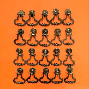 May include: Twenty antique brass cabinet knobs with a heart-shaped design. The knobs are arranged in four rows of five on a bright orange background.