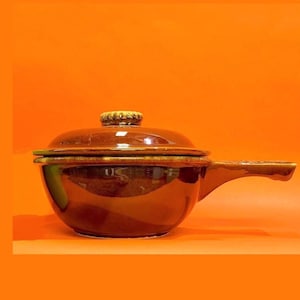May include: A brown ceramic casserole dish with a lid and a single handle. The dish has a glazed finish and a slightly rounded shape.