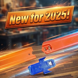 May include: Image features orange toy track pieces and a blue connector, with the text "New for 2025!". The track pieces are on a wooden surface, with a blurred workshop background. The image has a dynamic, energetic feel.