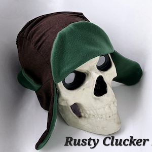 May include: A brown and green winter hat with ear flaps. The hat is worn on a white skull with black eye sockets.