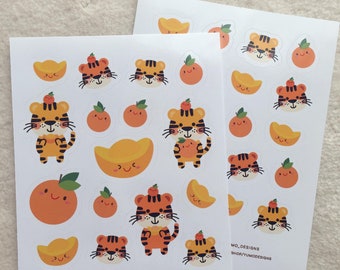 May include: A sheet of stickers featuring cute cartoon tigers with orange and gold accents. The stickers are perfect for adding a touch of whimsy to your planner, journal, or laptop. The stickers feature the text "Yumo Designs" and "@yumo.designs".
