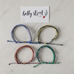 May include: Four colorful friendship bracelets made of woven string. The bracelets are blue, yellow, red, and green.